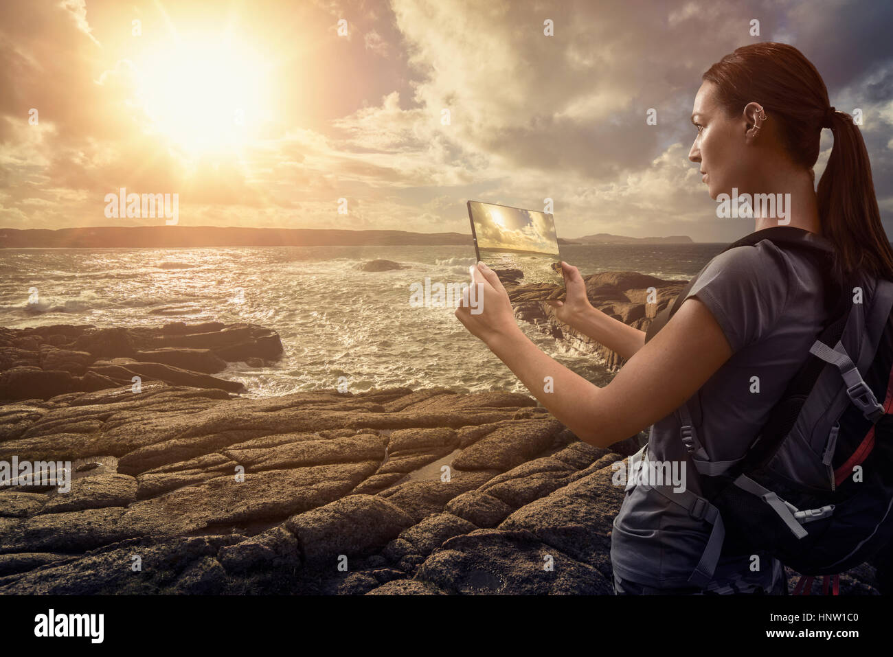 Caucasian woman photographing ocean sunset with digital tablet Stock Photo