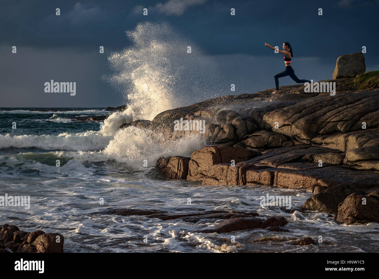 Distant Caucasian woman doing yoga on rocks near ocean Stock Photo