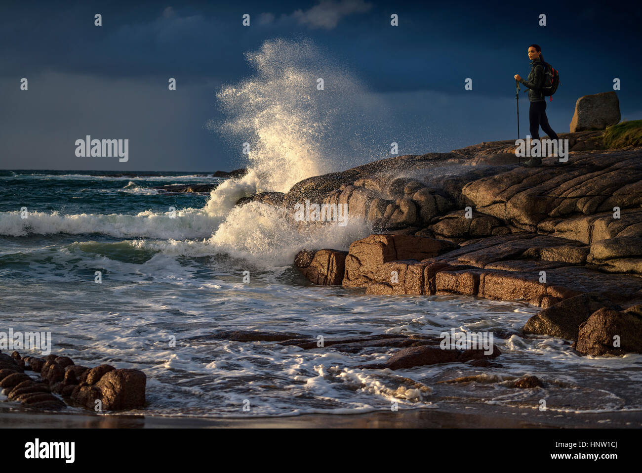 Distant Caucasian woman hiking on rocks near ocean Stock Photo