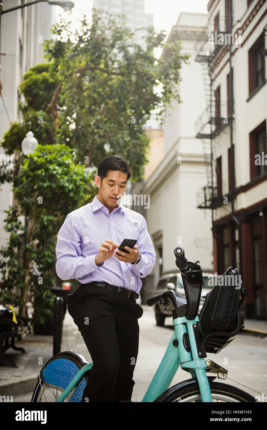 Chinese businessman on bicycle texting on cell phone Stock Photo