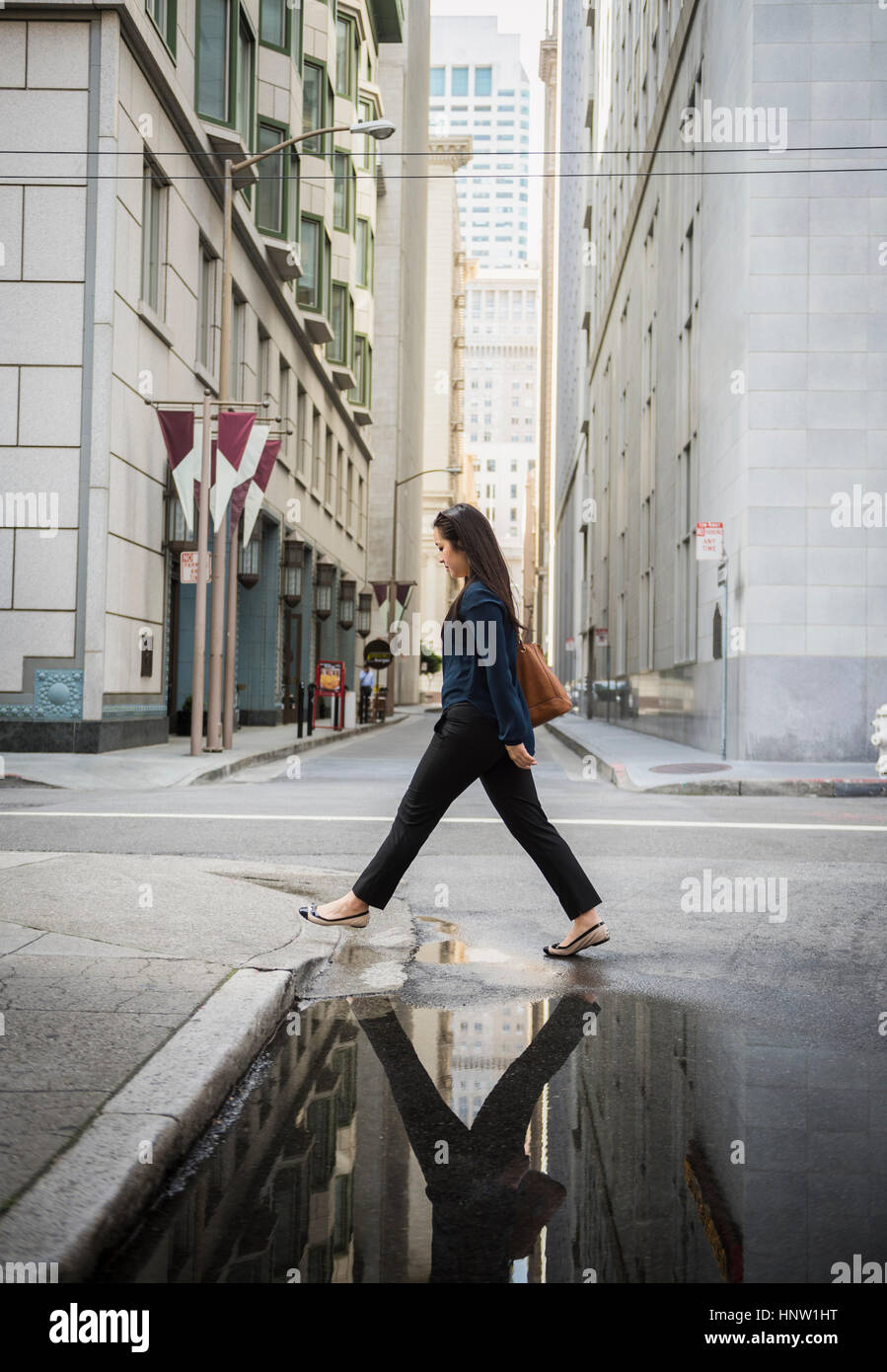 Reflection in puddle of Chinese businesswoman crossing street Stock Photo