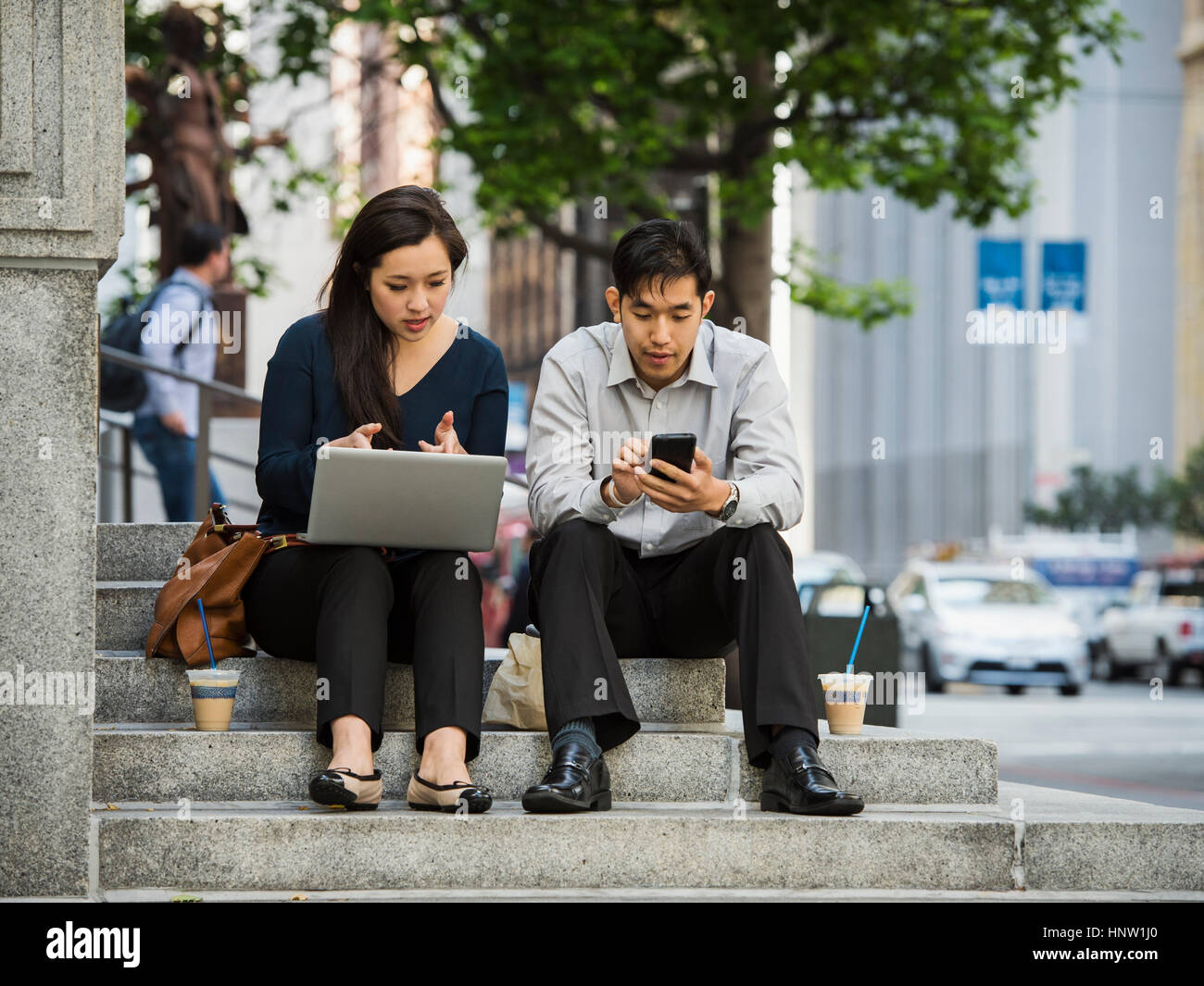 Chinese business people using technology during lunch in city Stock Photo