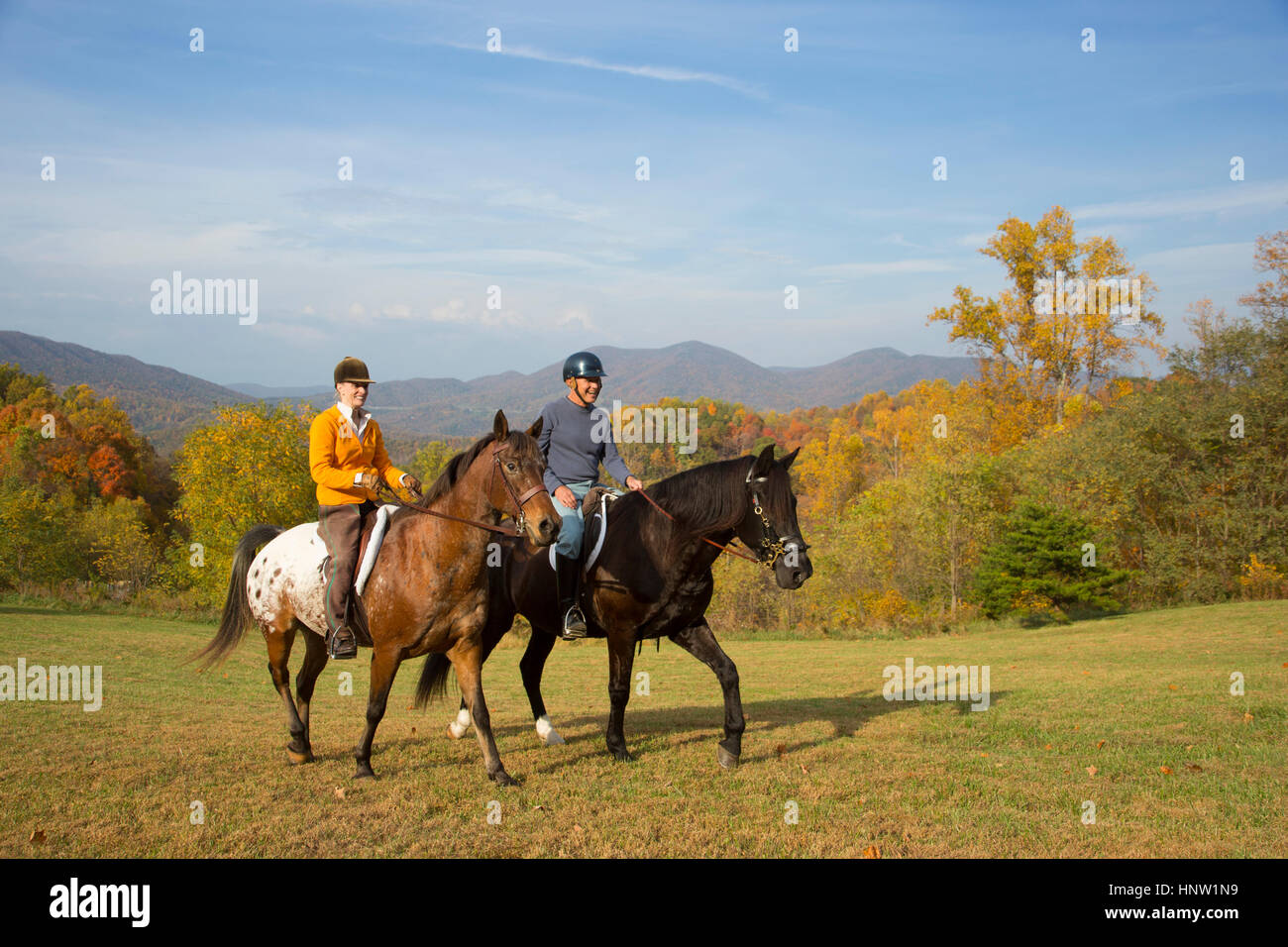 Older Caucasian couple horseback riding in field Stock Photo