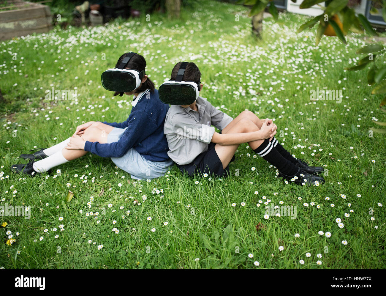 Mixed Race brother and sister sitting in grass wearing virtual reality goggles Stock Photo