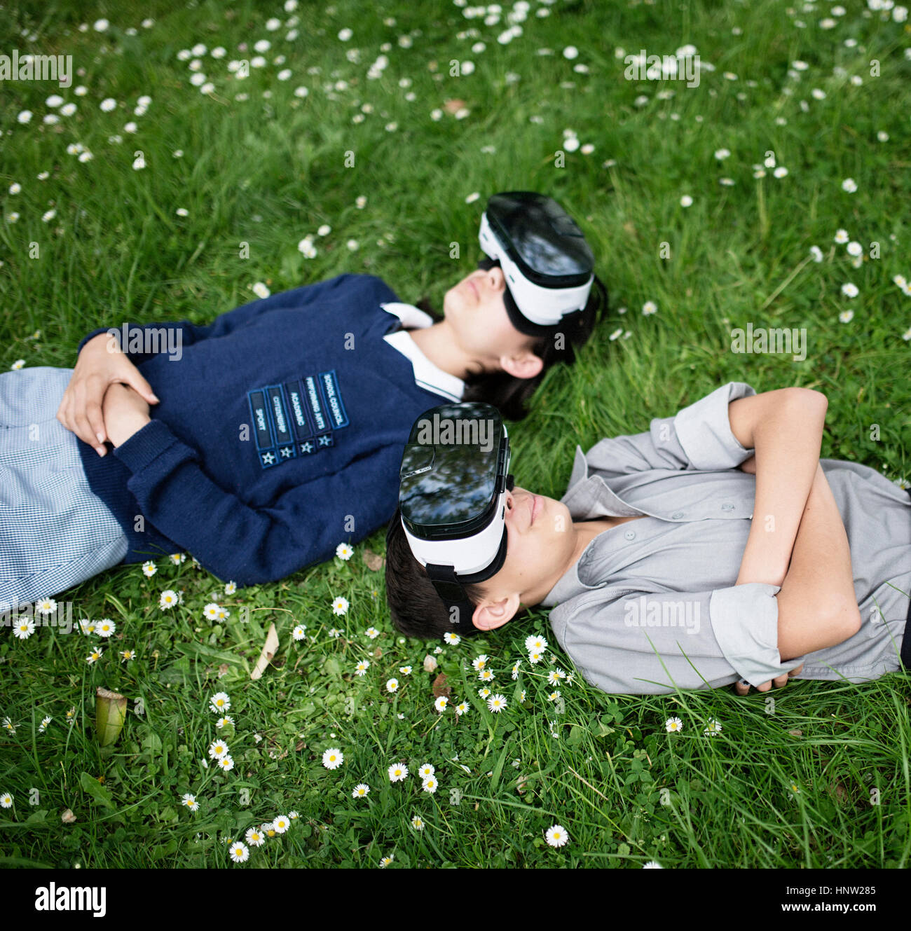 Mixed Race brother and sister laying in grass wearing virtual reality goggles Stock Photo