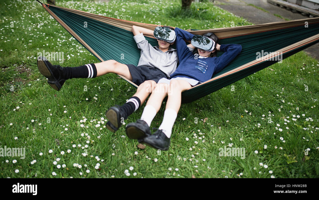 Mixed Race brother and sister in hammock wearing virtual reality goggles Stock Photo