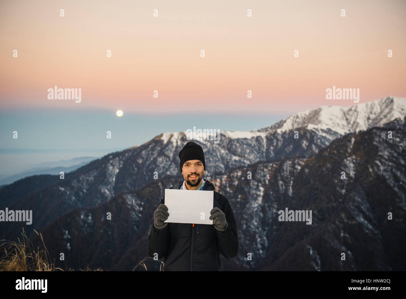 Smiling Caucasian man holding blank sign in mountain landscape Stock Photo