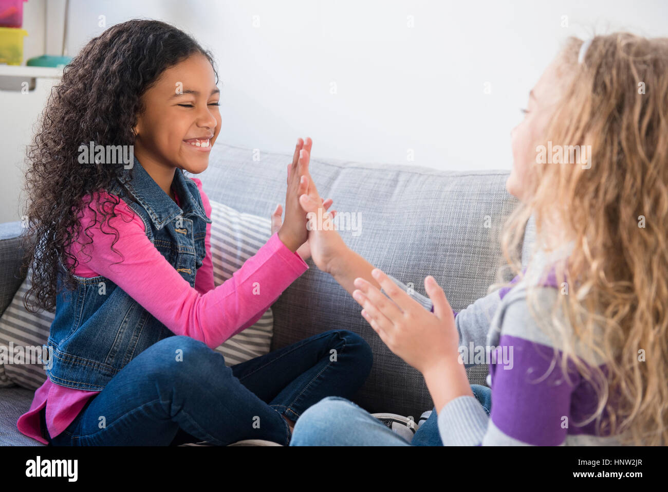 Smiling girls playing clapping game on sofa Stock Photo