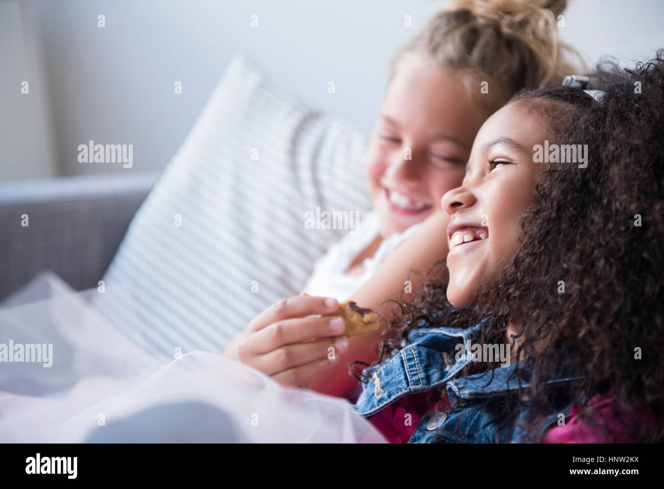 Smiling girls eating cookie on sofa Stock Photo