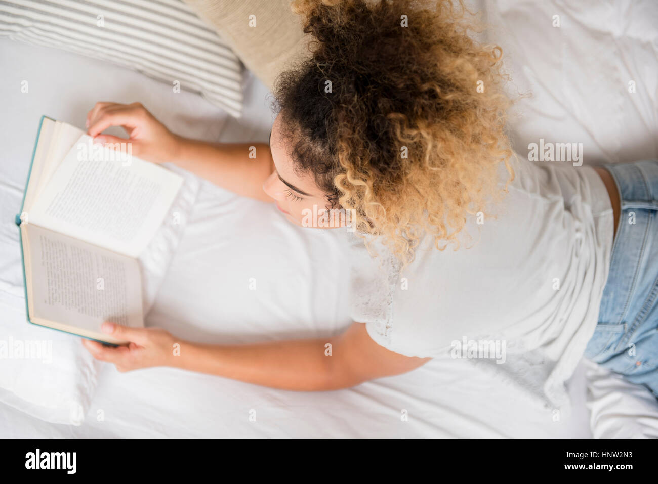 Mixed Race woman laying on bed reading book Stock Photo
