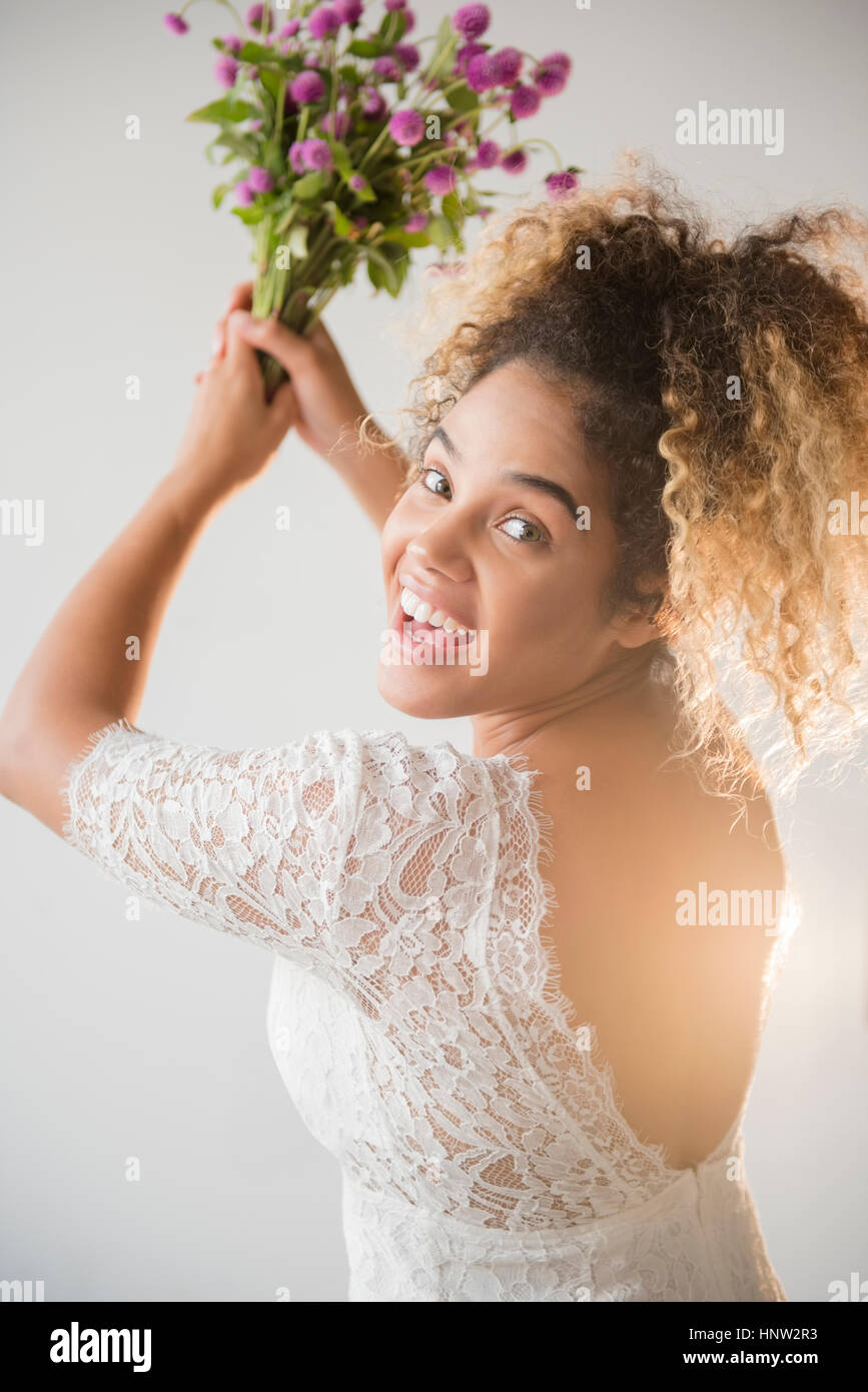 Mixed Race woman wearing wedding dress tossing bouquet Stock Photo