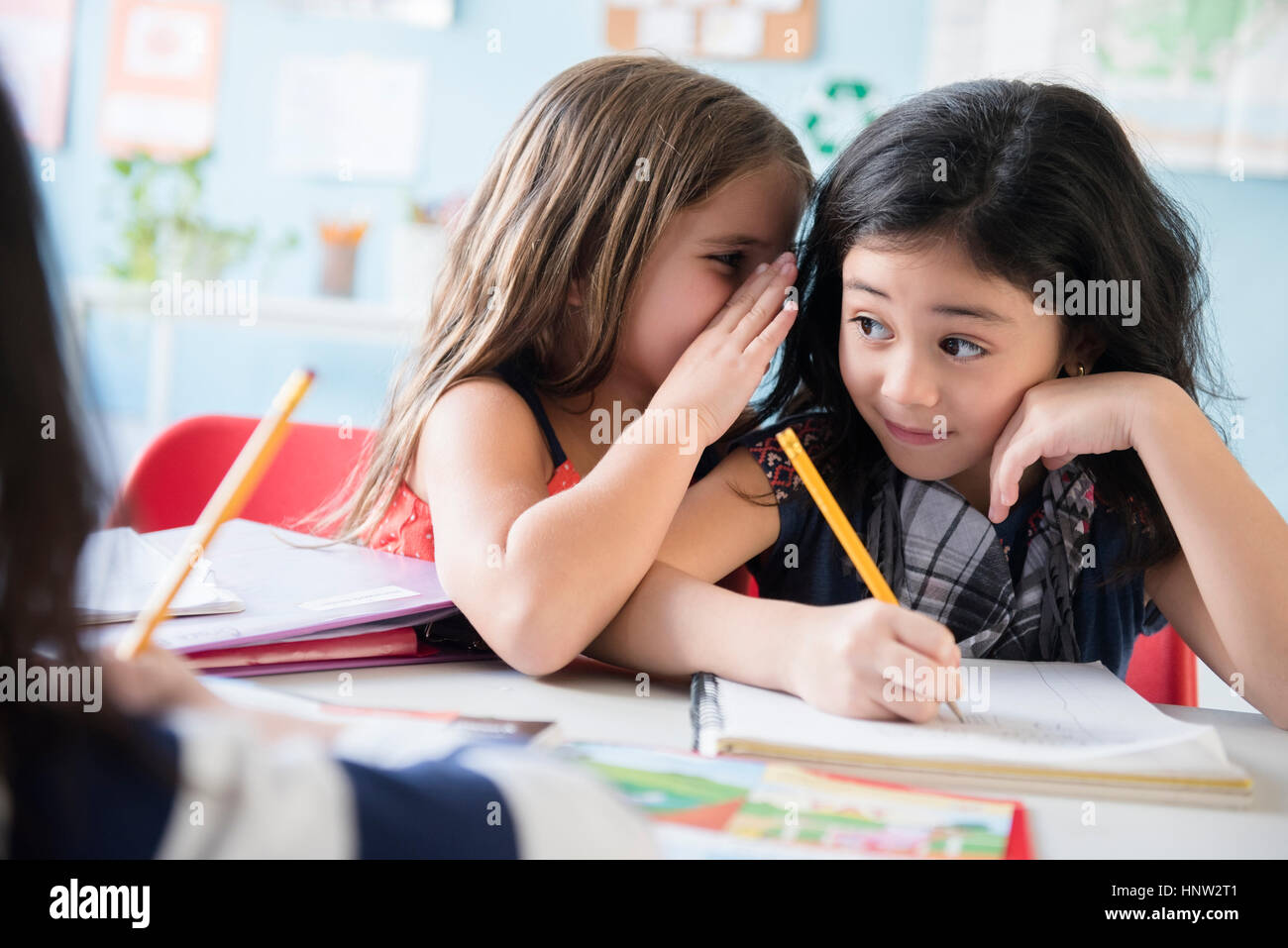 Girl whispering to classmate in school Stock Photo