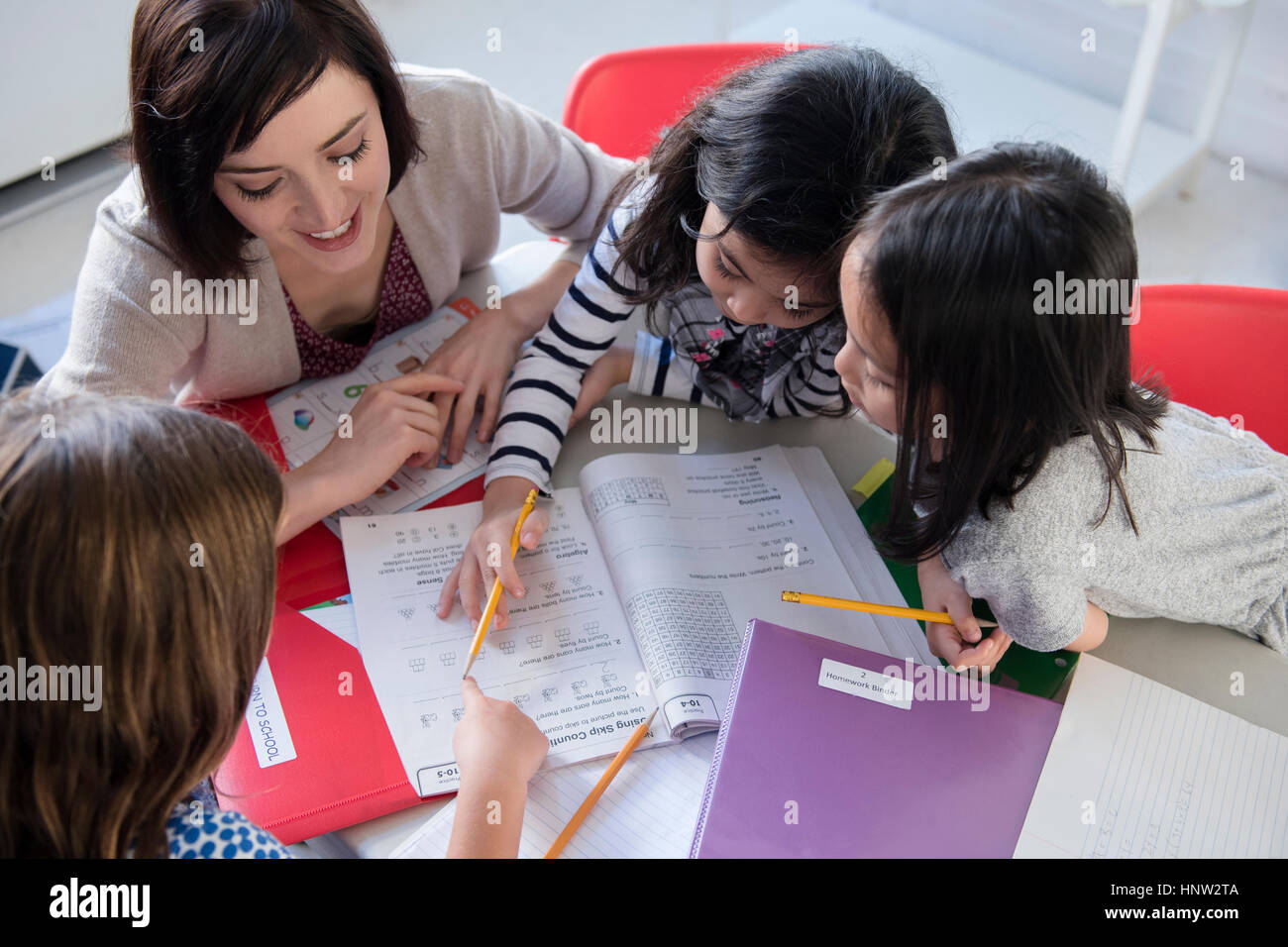Teacher helping girls with workbook in classroom Stock Photo