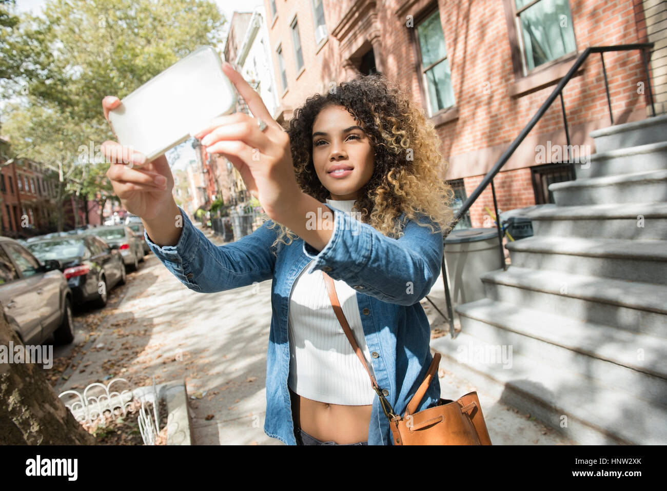 Mixed Race woman in city posing for cell phone selfie Stock Photo