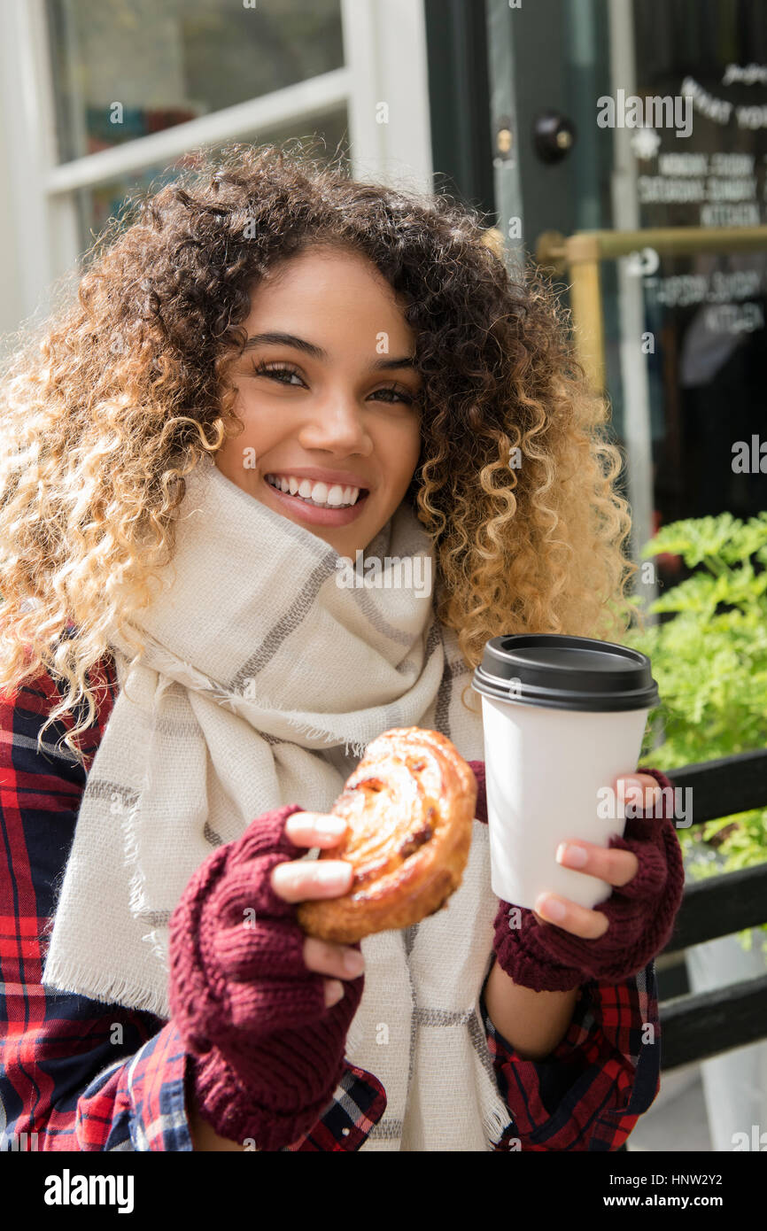 Smiling Mixed Race woman showing donut and coffee cup Stock Photo