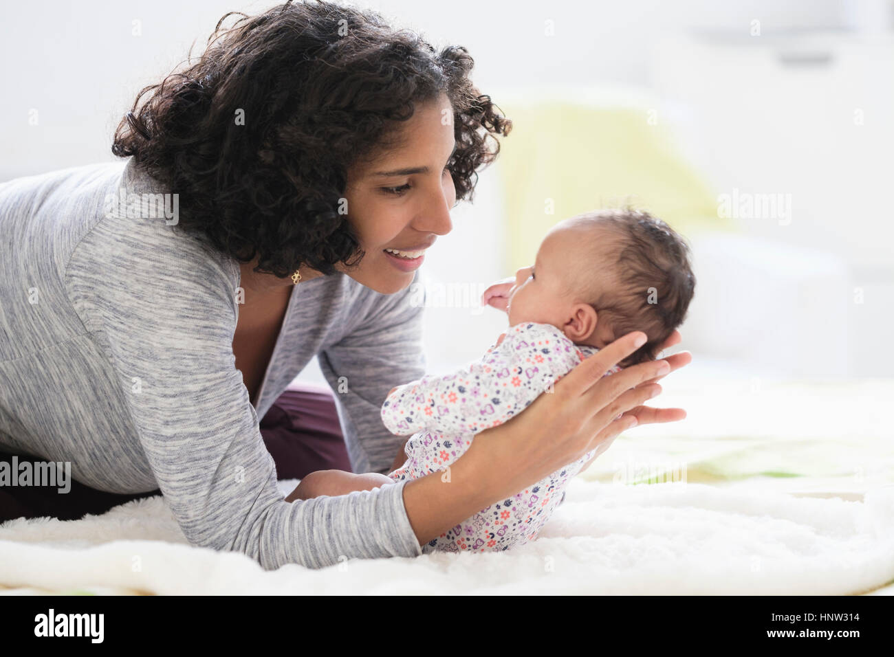 Hispanic mother laying on bed holding baby daughter Stock Photo