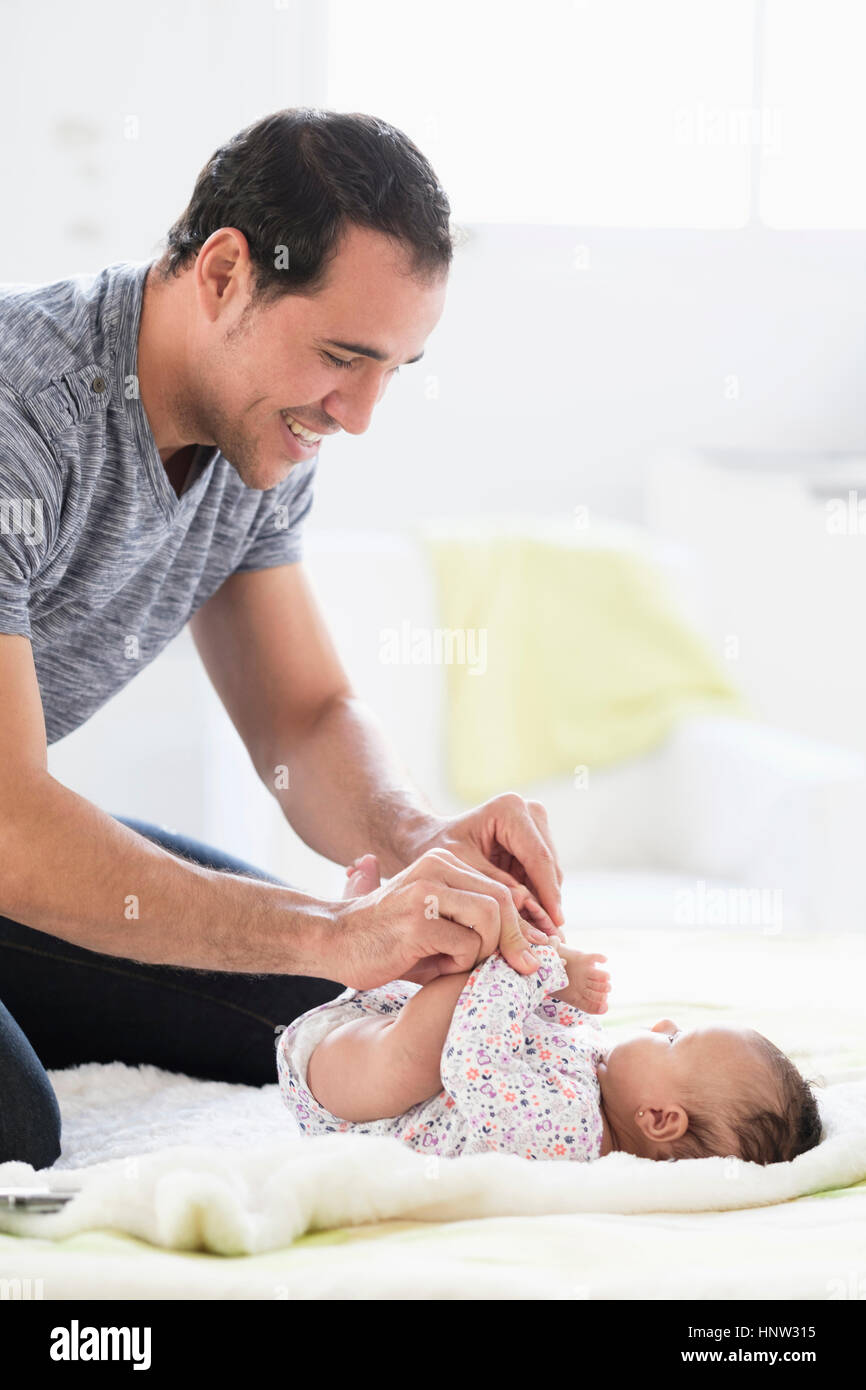 Hispanic father on bed playing with baby daughter Stock Photo