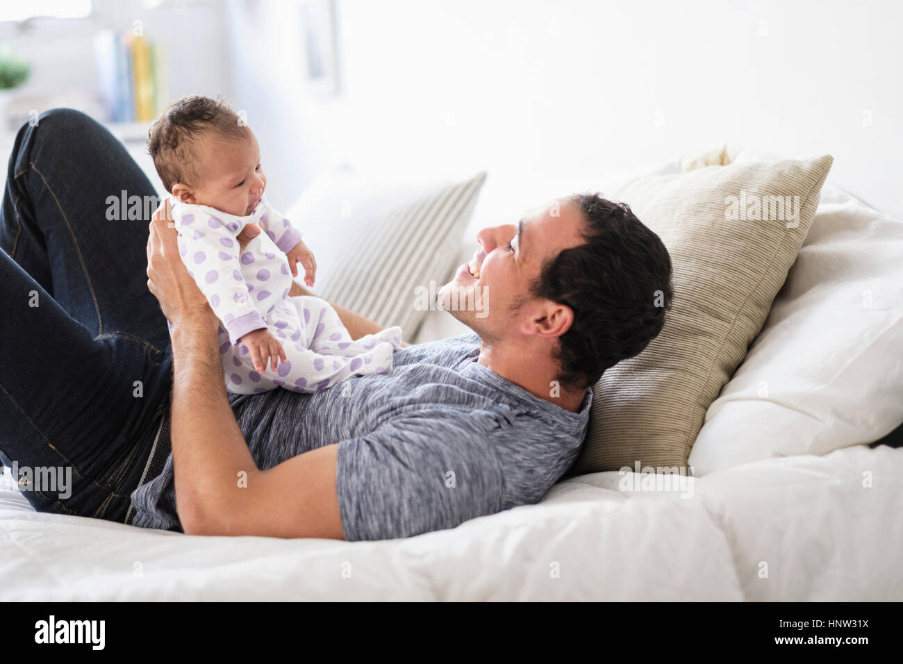 Hispanic father playing with baby daughter on bed Stock Photo
