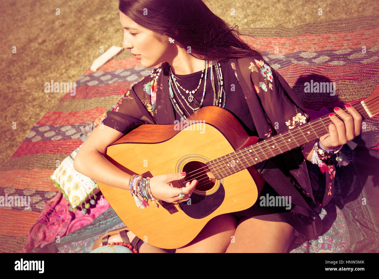 Asian woman sitting on blanket playing guitar Stock Photo