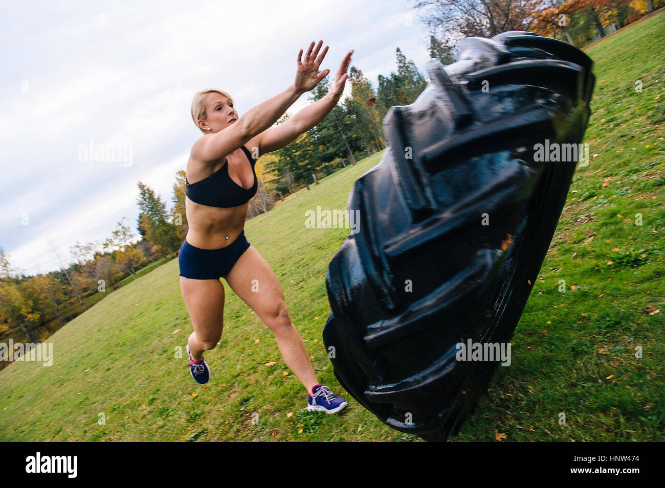 Caucasian woman pushing heavy tire up hill Stock Photo