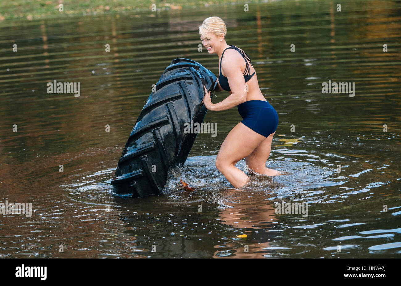 Caucasian woman pushing heavy tire in lake Stock Photo