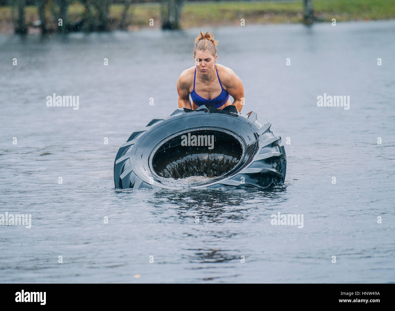 Caucasian woman lifting heavy tire in lake Stock Photo