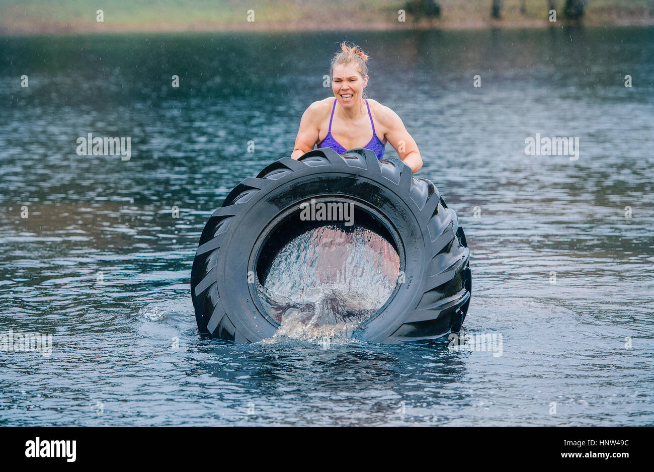 Caucasian woman pushing heavy tire in lake Stock Photo