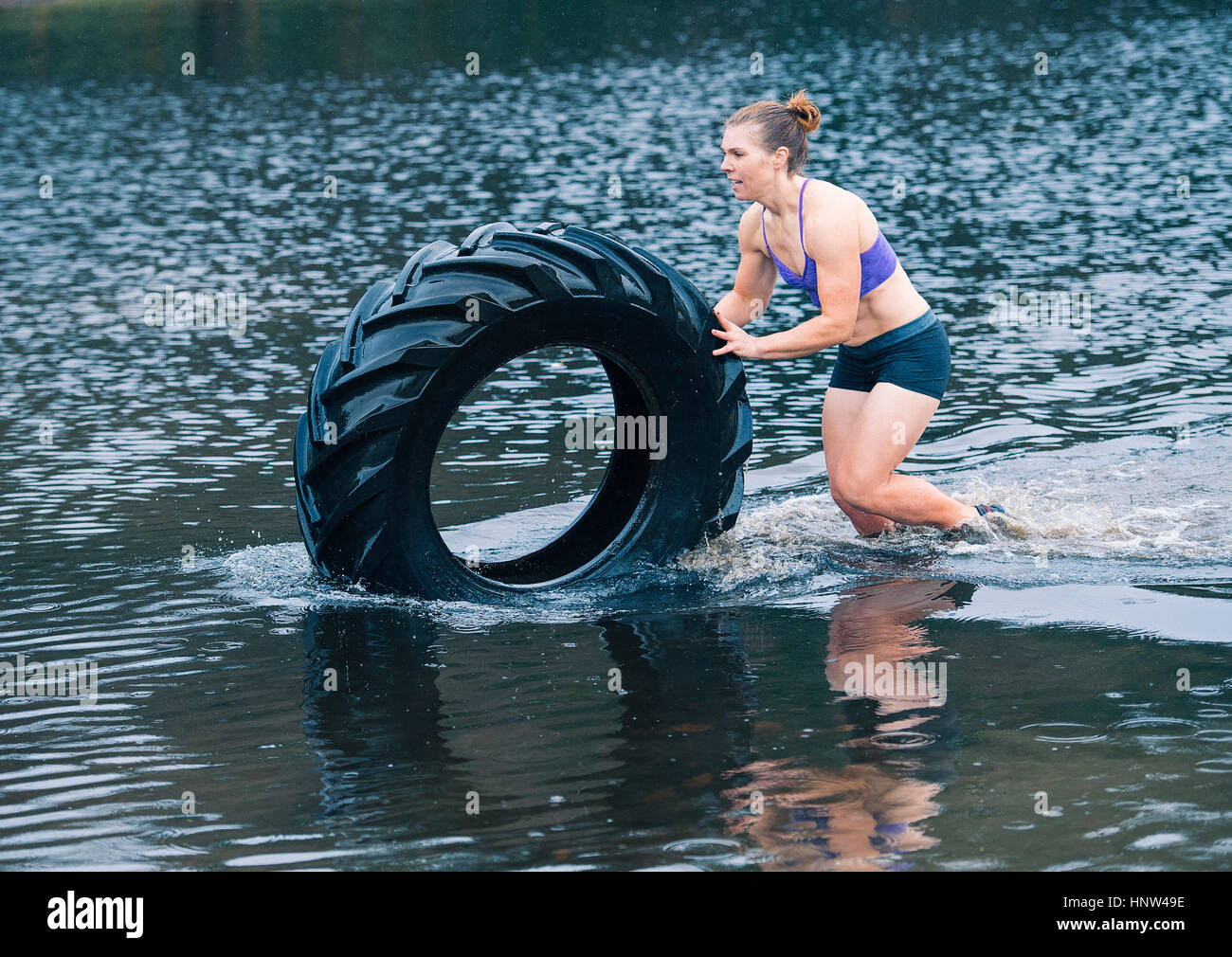Caucasian woman pushing heavy tire in lake Stock Photo