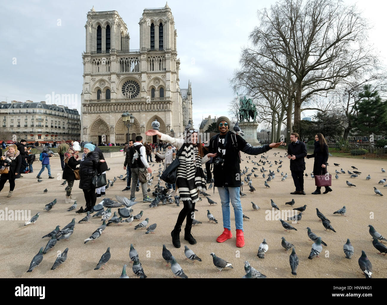 A young couple pose for pictures as they feed pigeons outside the Notre Dame Cathedral in Paris, France Stock Photo