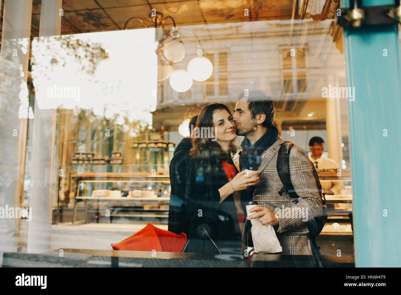 Caucasian man kissing woman on cheek behind bakery window Stock Photo