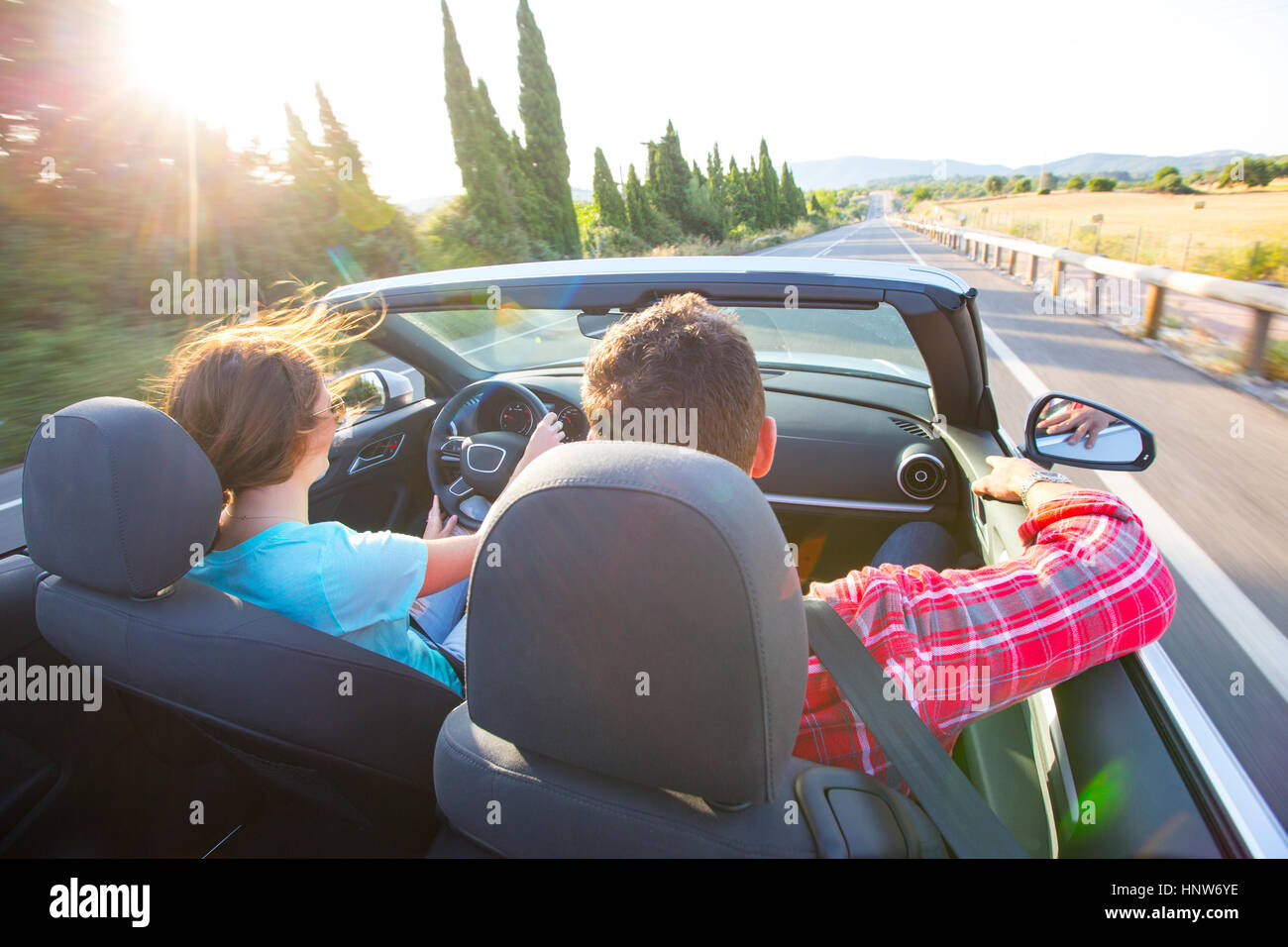 Rear view of couple driving convertible on sunlit rural road, Majorca, Spain Stock Photo