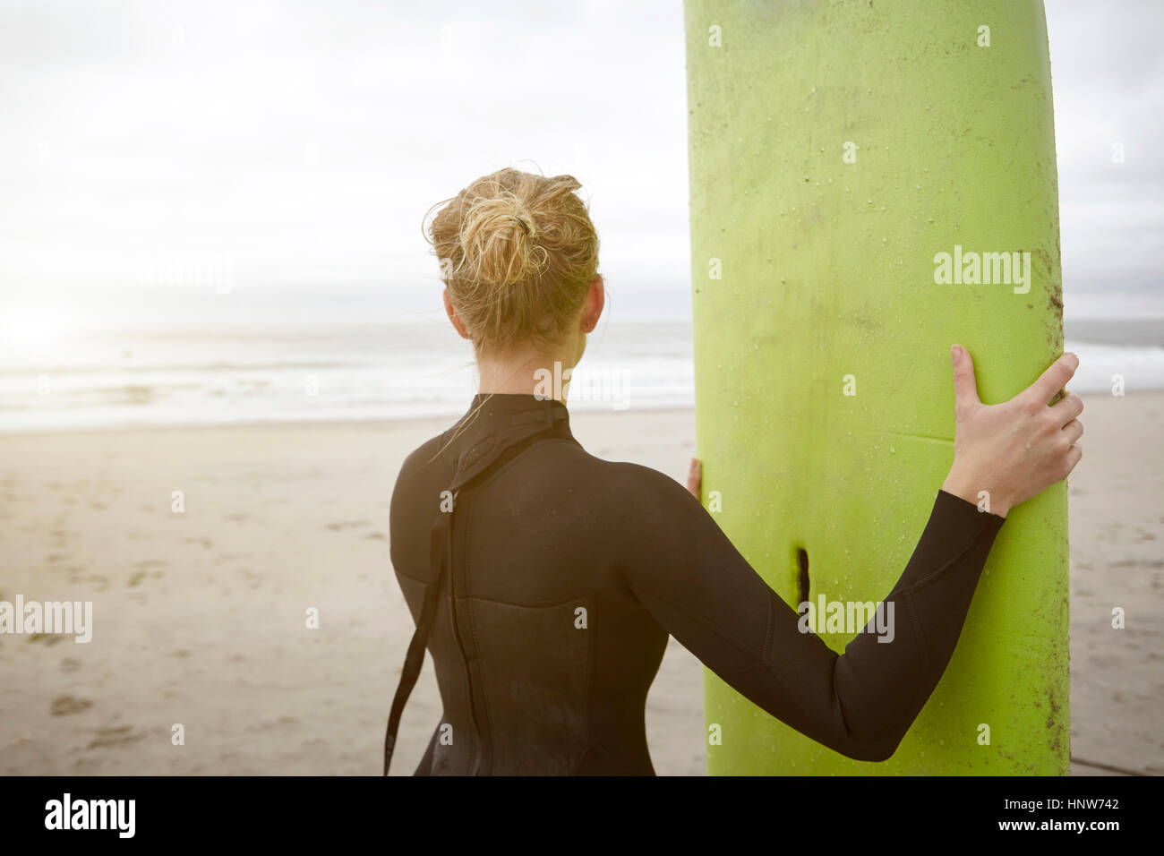 Female surfer holding surfboard looking out from Rockaway Beach, New York, USA Stock Photo