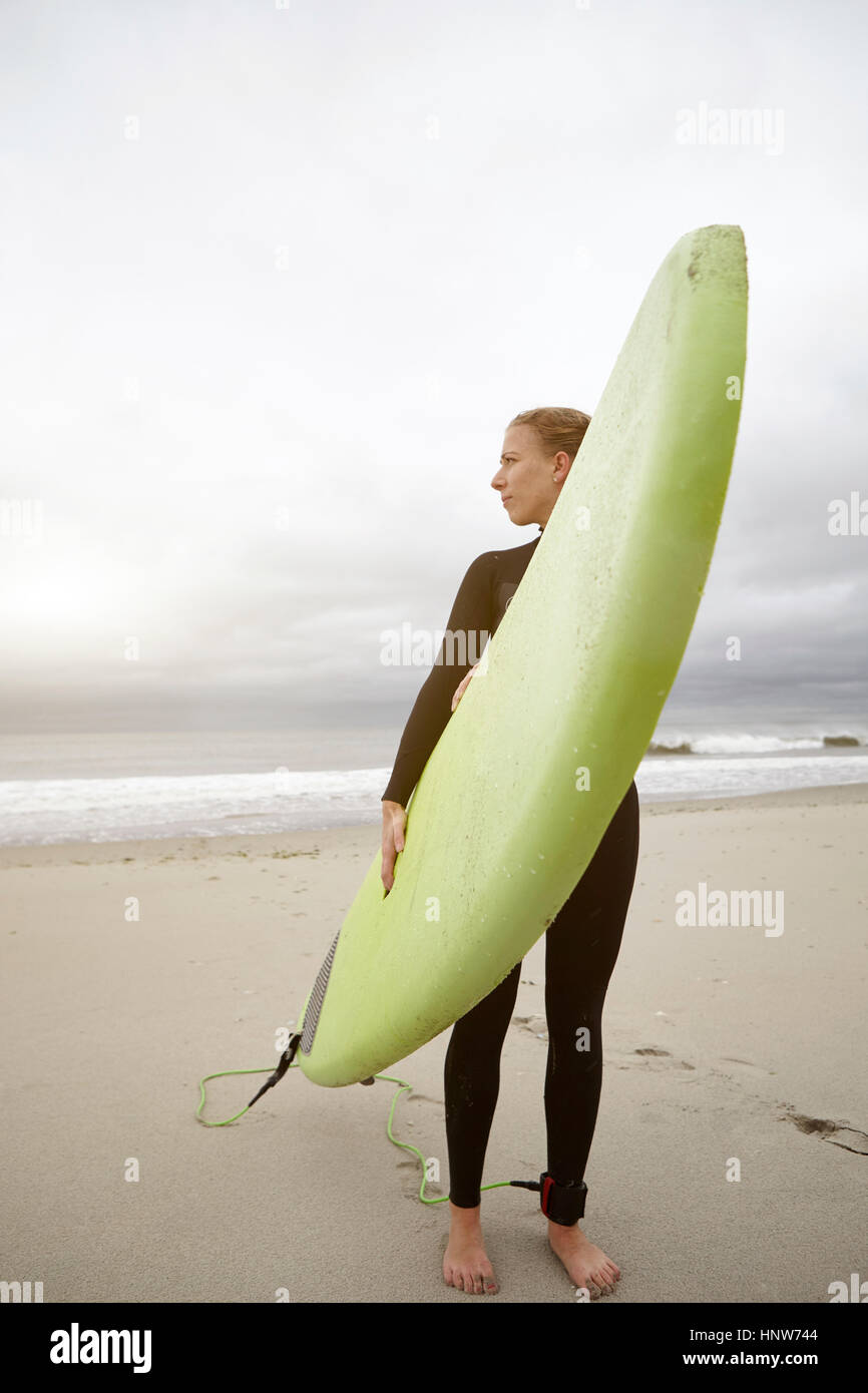 Female surfer carrying surfboard looking back from Rockaway Beach, New York, USA Stock Photo