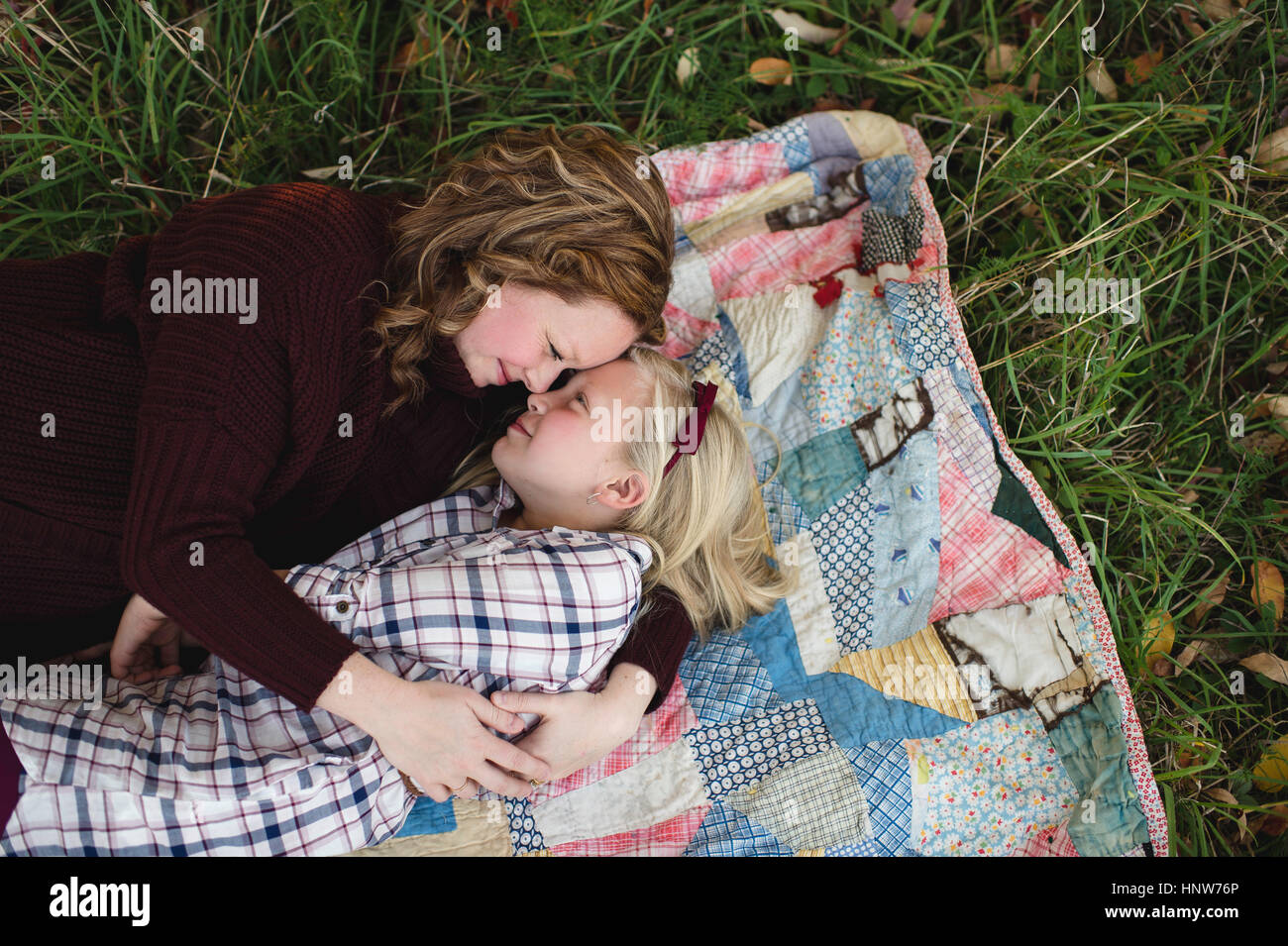 Mother and daughter lying on blanket face to face hugging Stock Photo
