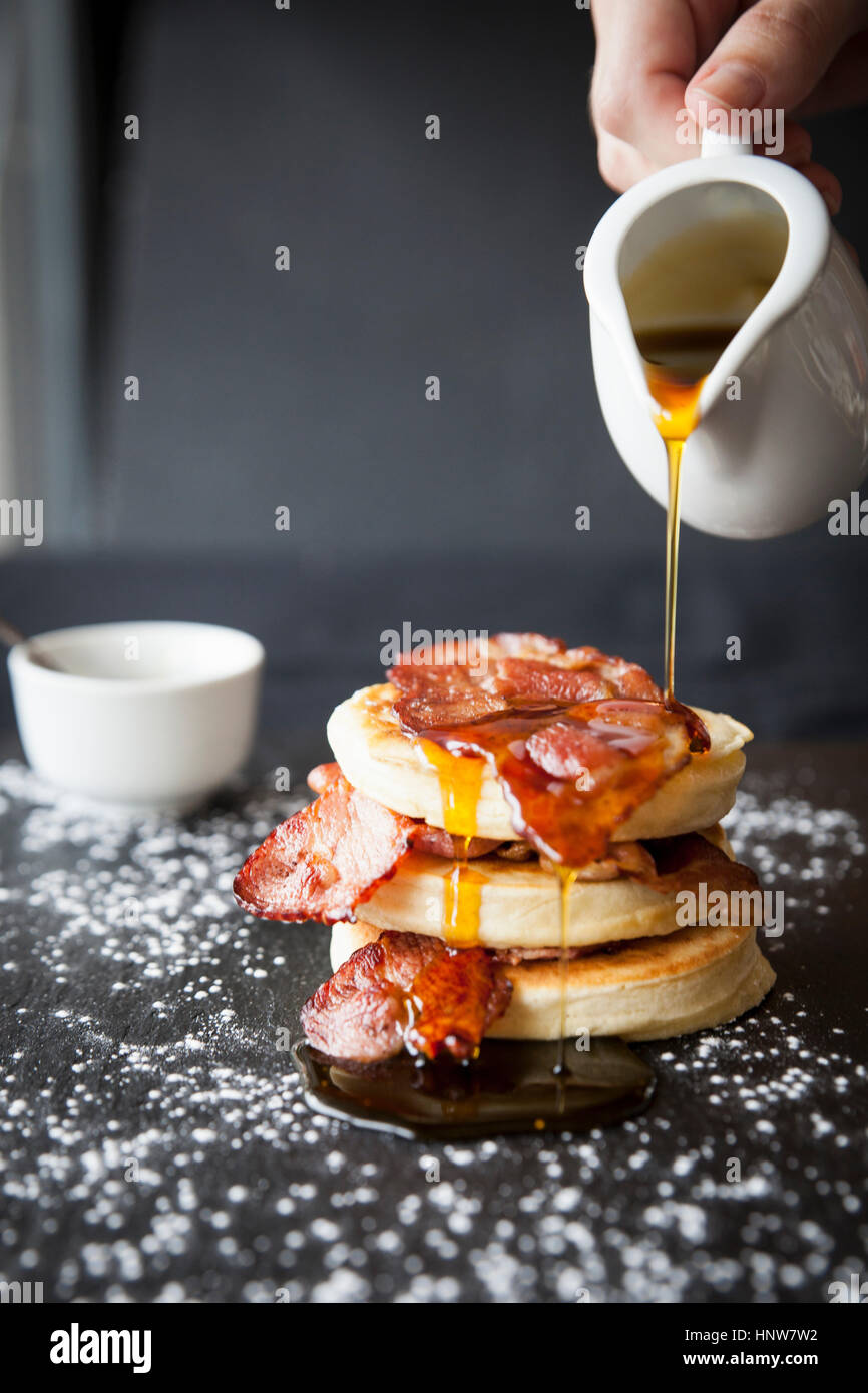 Female hand pouring maple syrup over breakfast bacon crumpet on slate Stock Photo