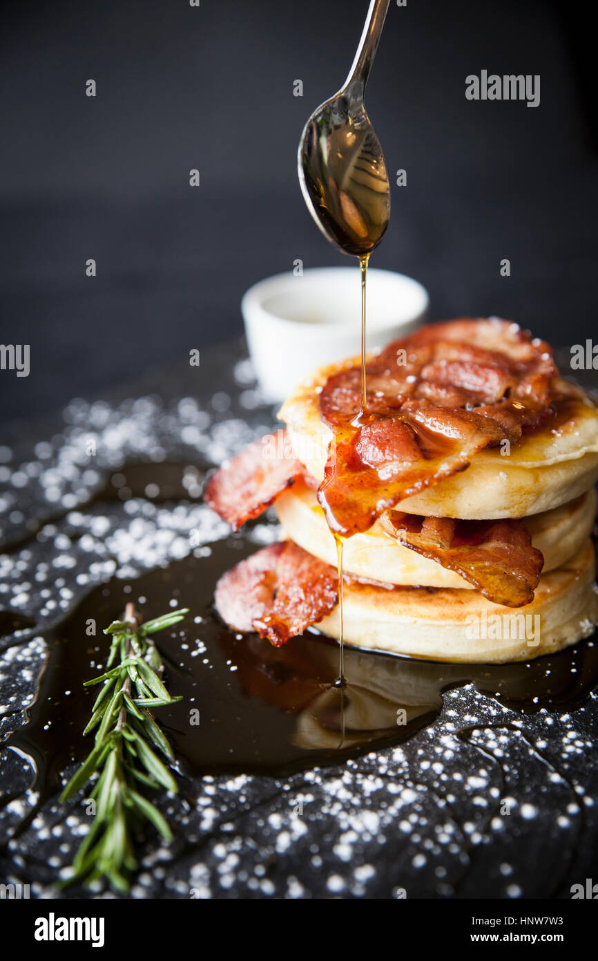 Breakfast bacon crumpet with maple syrup pouring from spoon onto slate Stock Photo