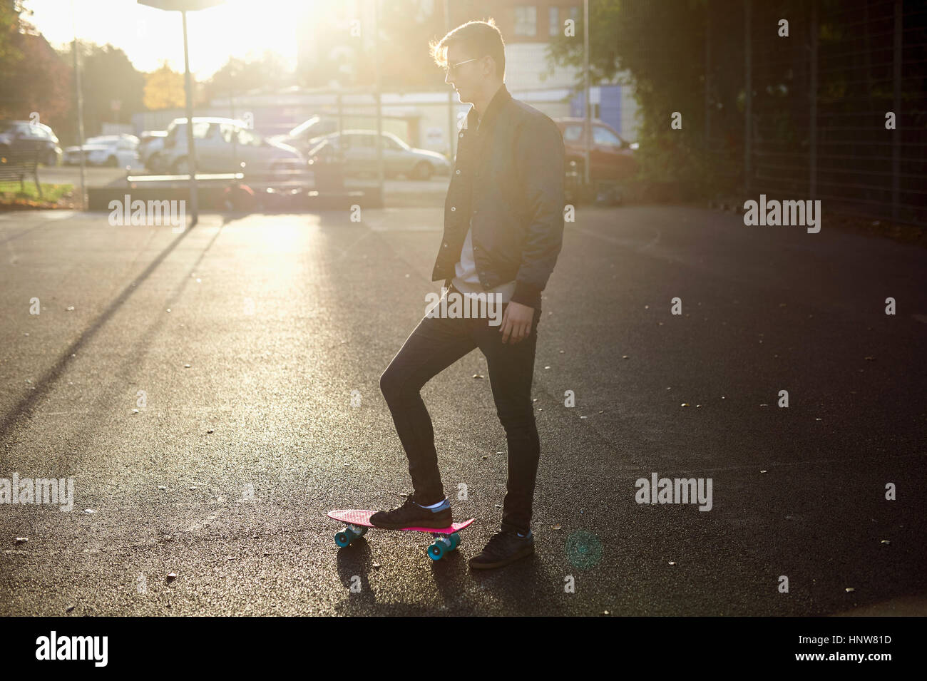 Young male skateboarder with skateboard on sunlit street Stock Photo
