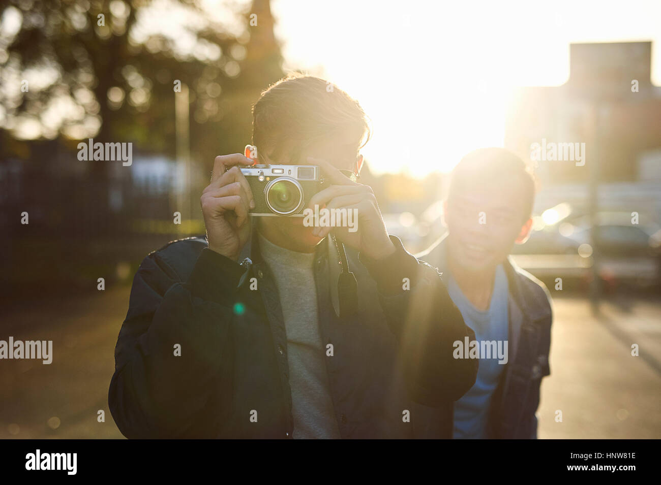 Young man taking camera photographs on sunlit street Stock Photo