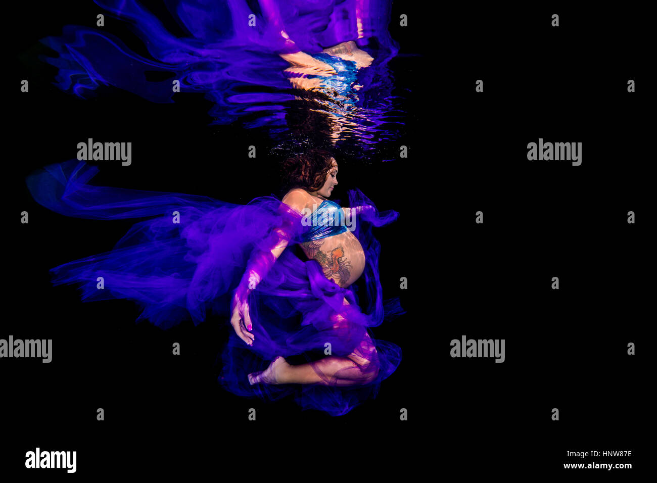 Pregnant woman draped in sheer fabric, underwater view Stock Photo