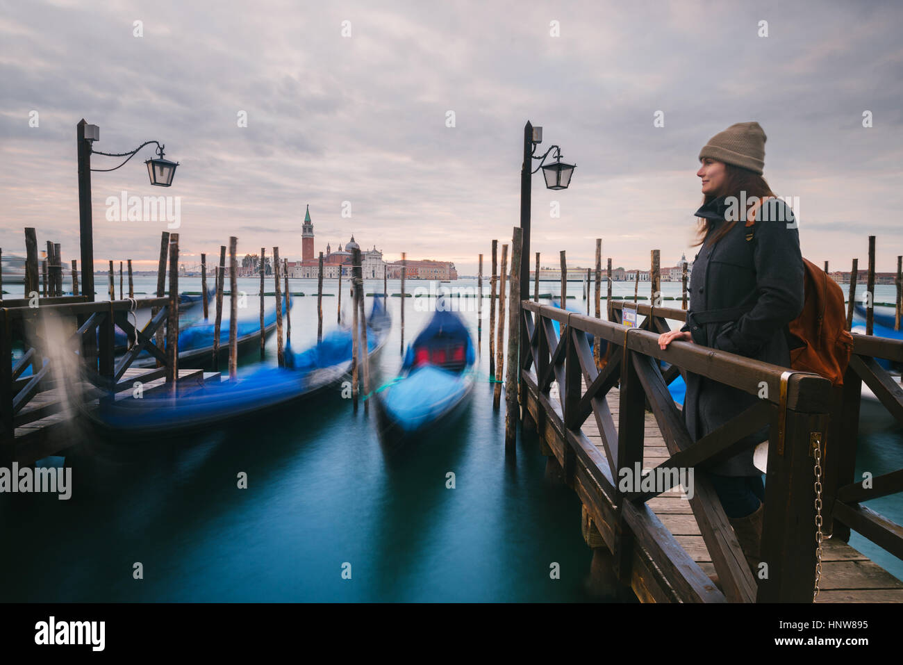 Woman on pier by gondolas in Grand Canal, San Giorgio Maggiore Island in background, Venice, Italy Stock Photo