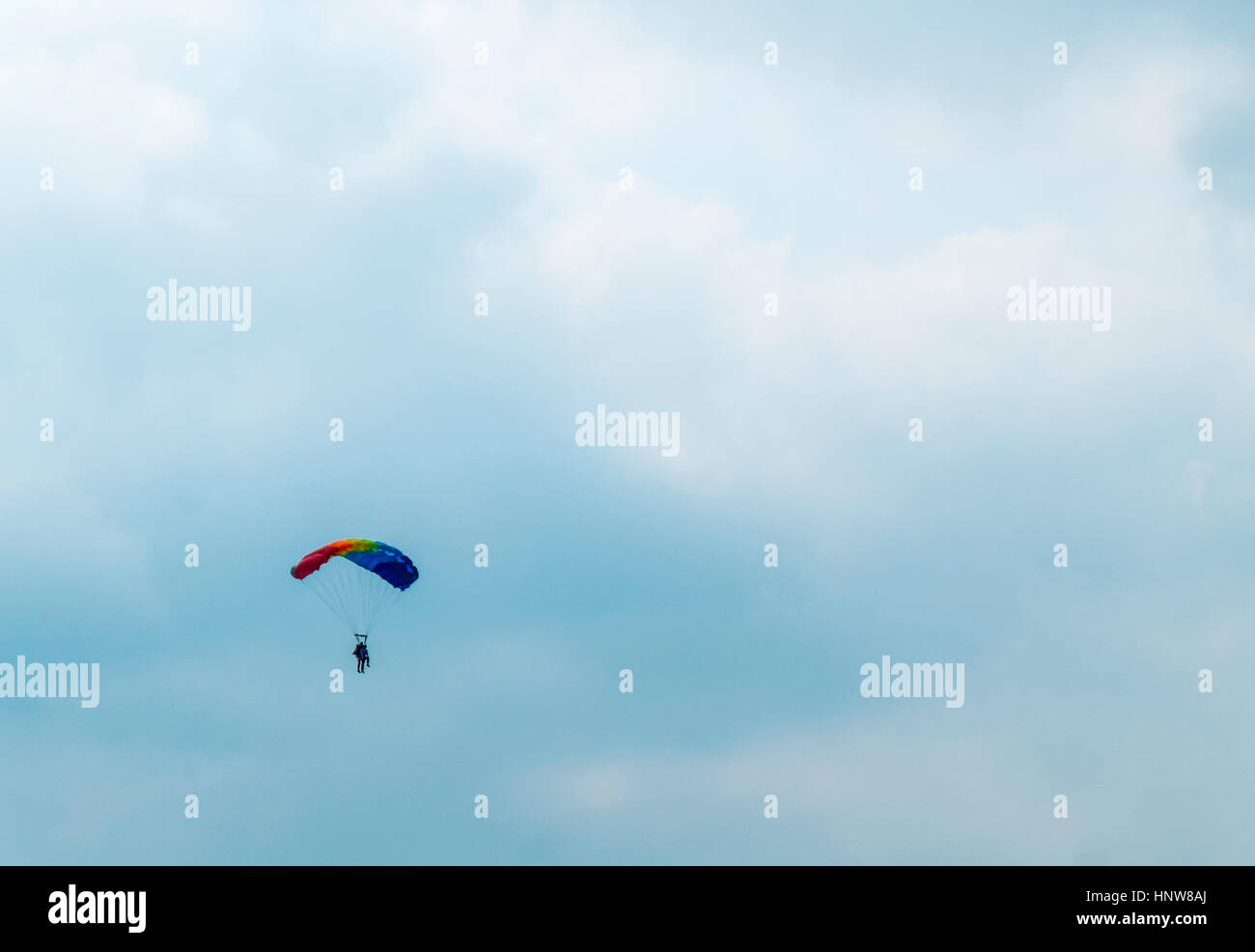 Distant view of man parachuting down against cloudy sky Stock Photo