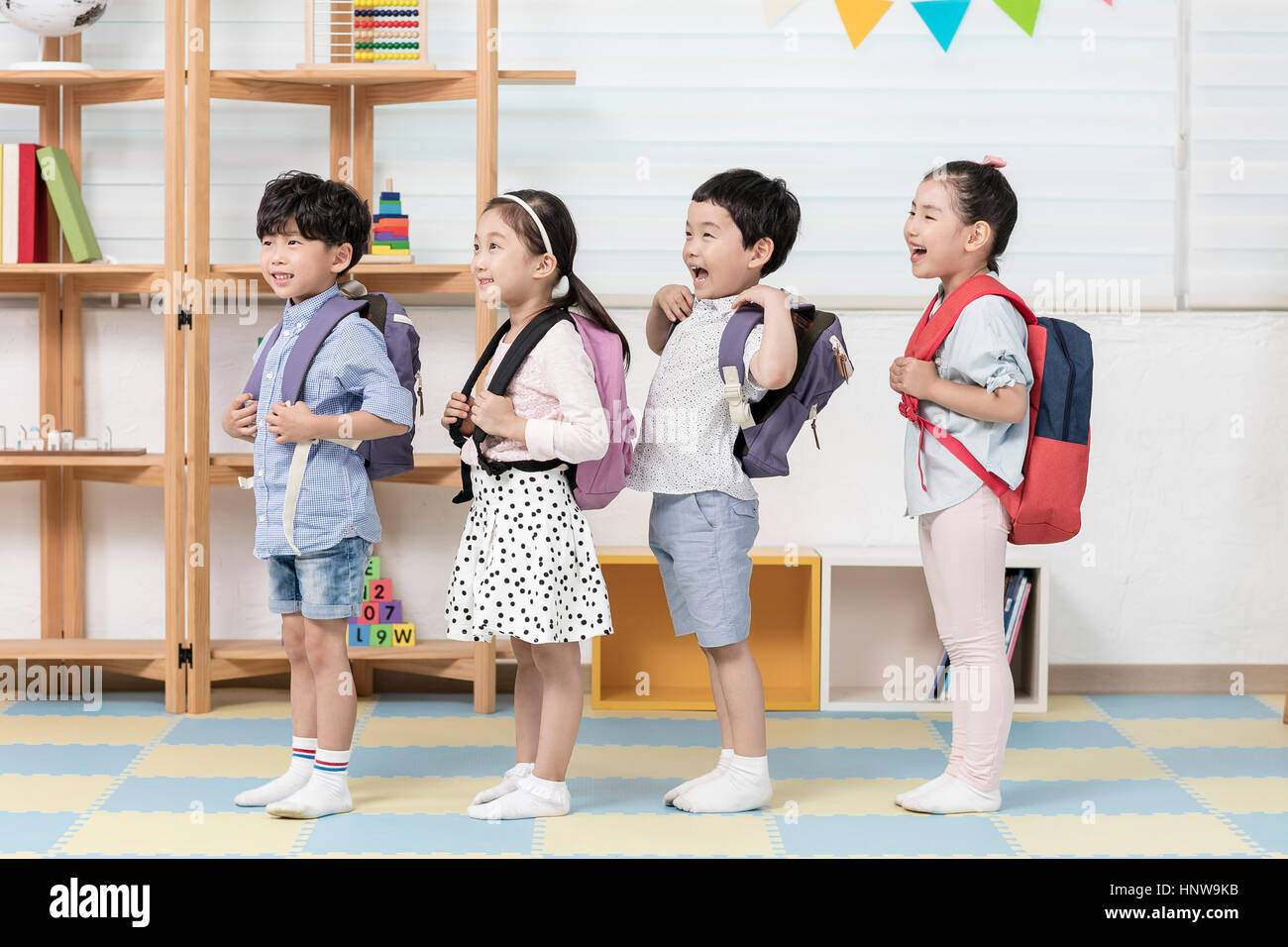 Smiling kindergarten children with backpacks lining up Stock Photo