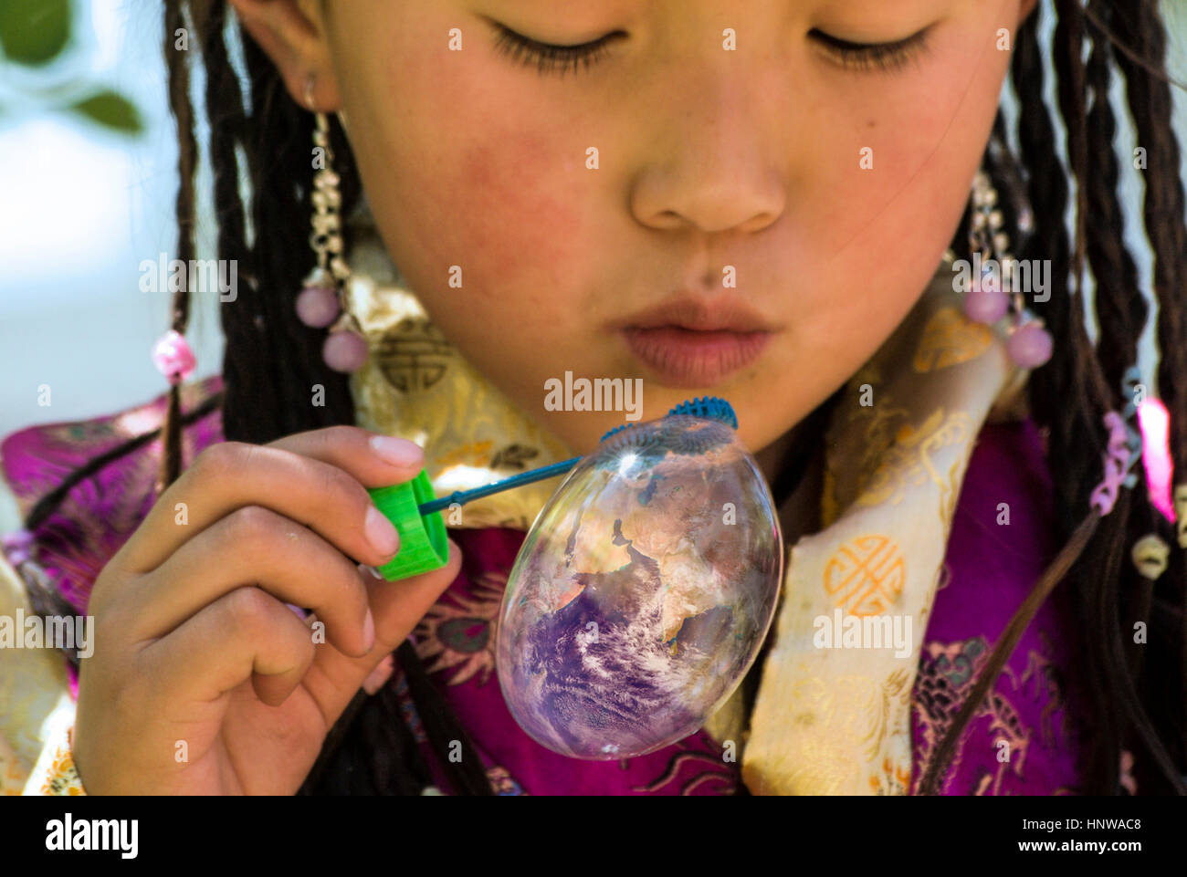 Photoshopped concept image with Young Tibetan Girl blowing up a soap bubble containing the Earth Stock Photo