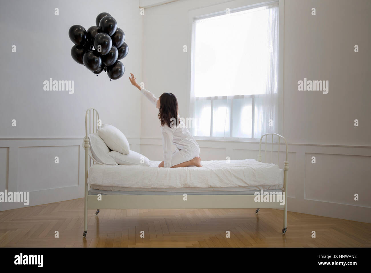 Young woman in bed reaching for black balloons Stock Photo