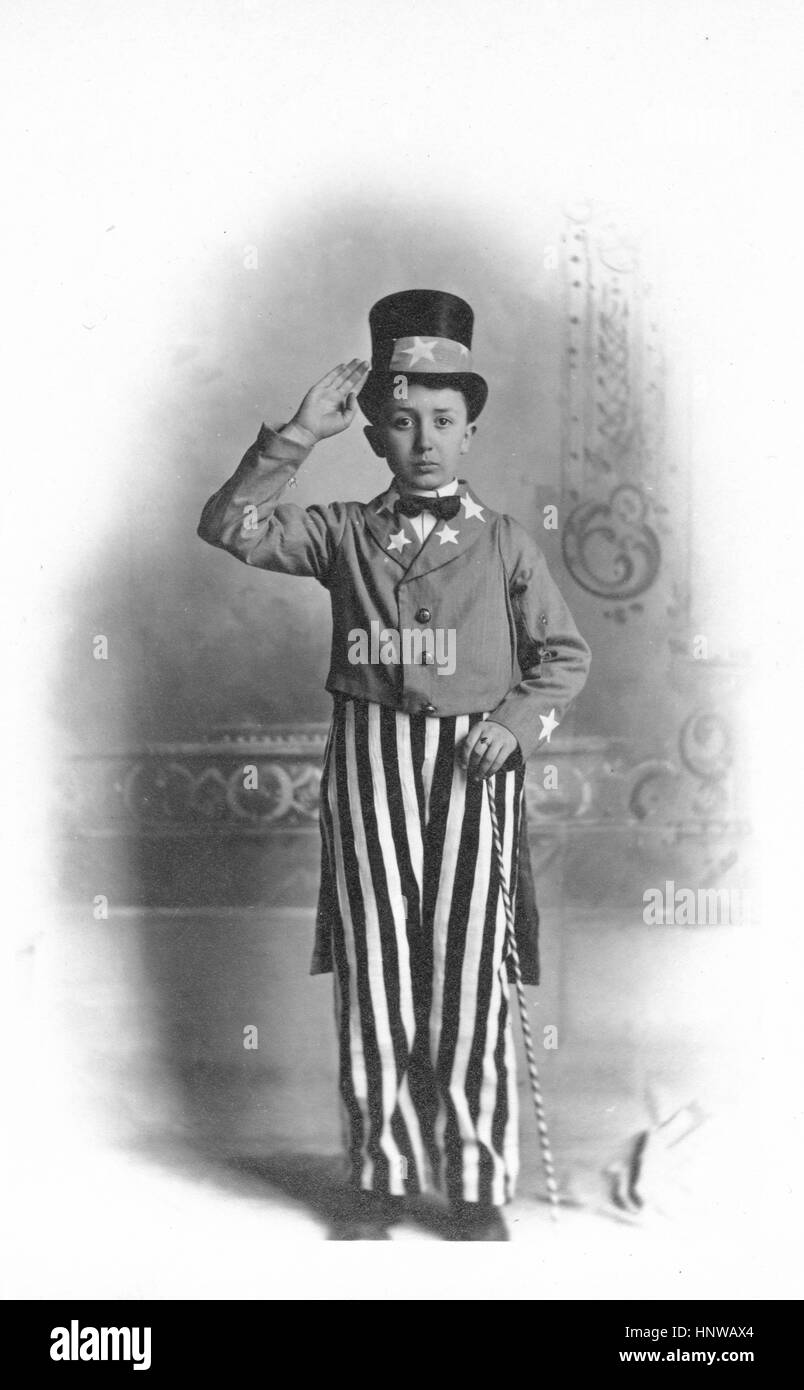 Young boy dressed up Very patriotically as Uncle Sam, c. 1910.  A great 4th of July costume.  He stands proud, saluting, and holding a thin, striped cane.  Star on his top hat and stars on his jacket.    To see my other holiday-related images, Search:  Prestor  vintage holiday Stock Photo