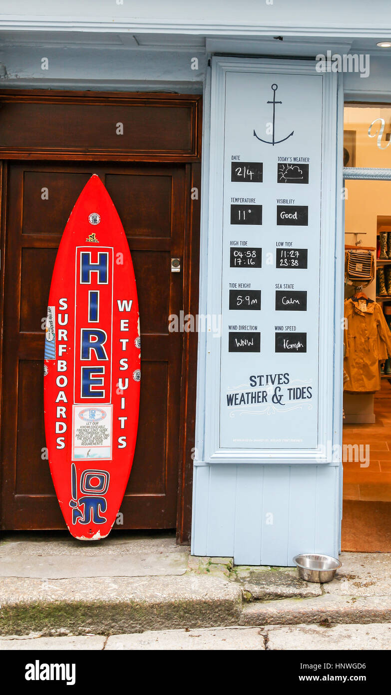 A surf board and a sign showing the weather and tides outside a shop in St. Ives, Cornwall, England, UK Stock Photo
