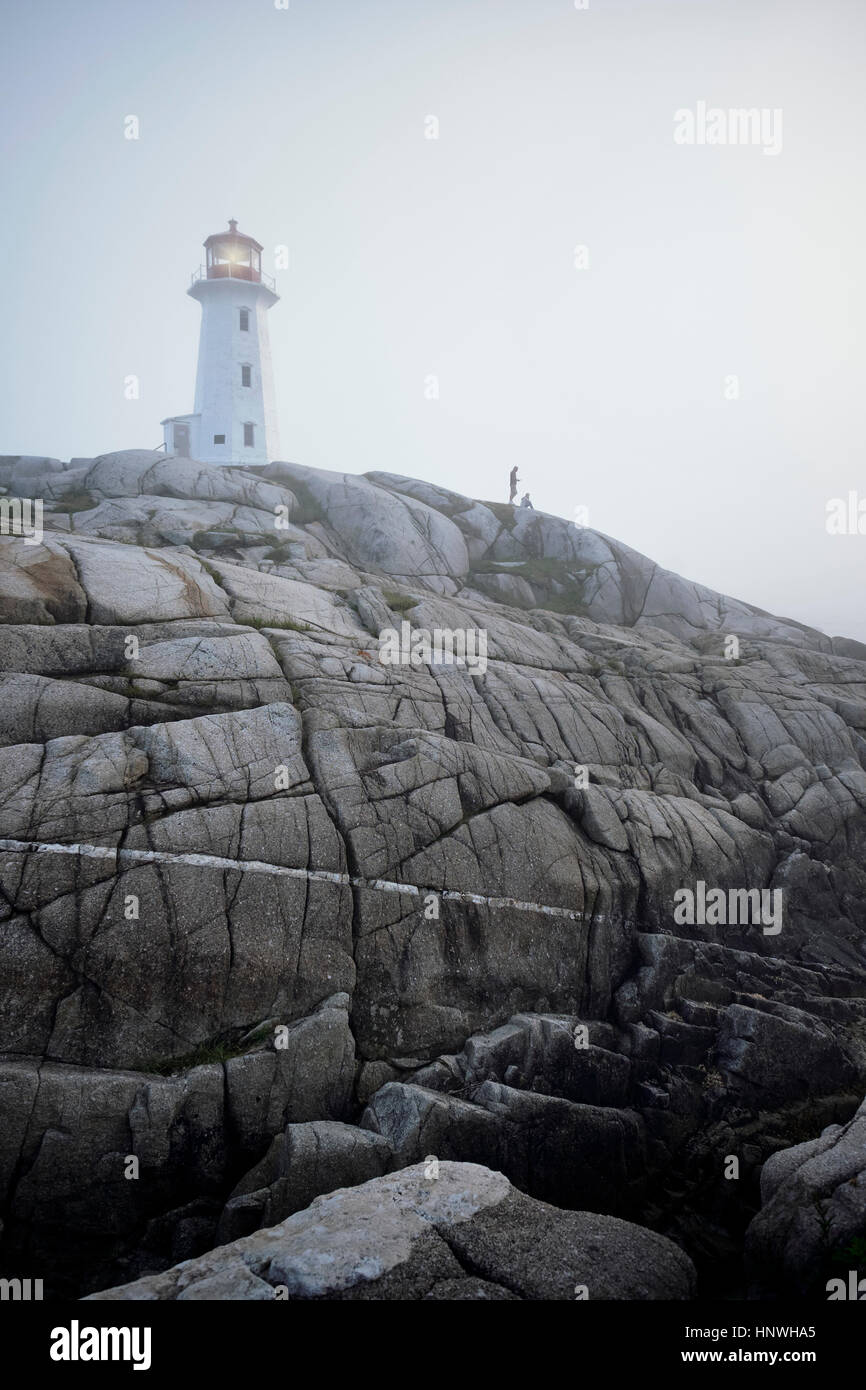 Couple on rocks by lighthouse, Peggy's Cove, Nova Scotia, Canada Stock Photo