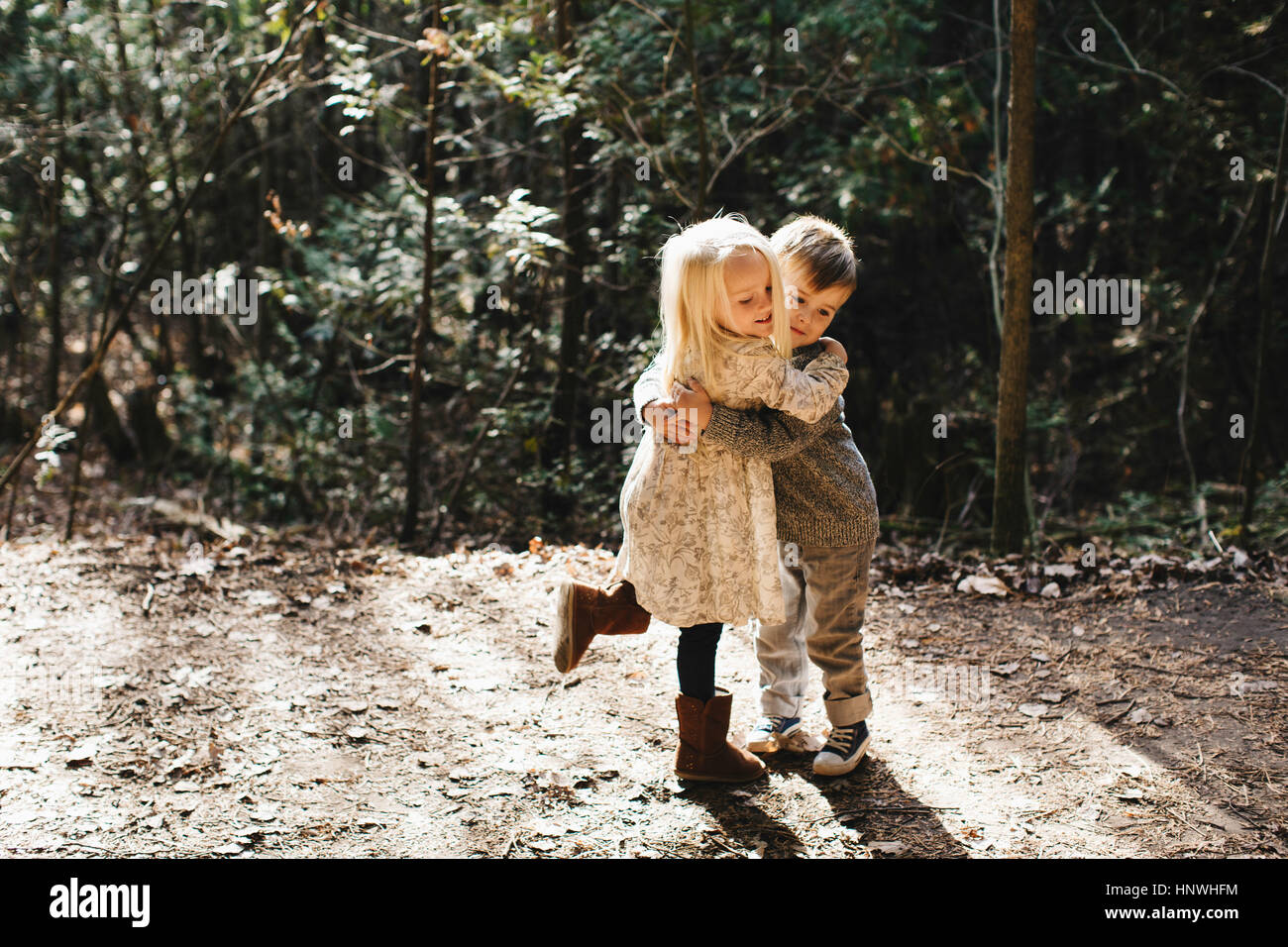 Siblings hugging and playing on gravel road Stock Photo