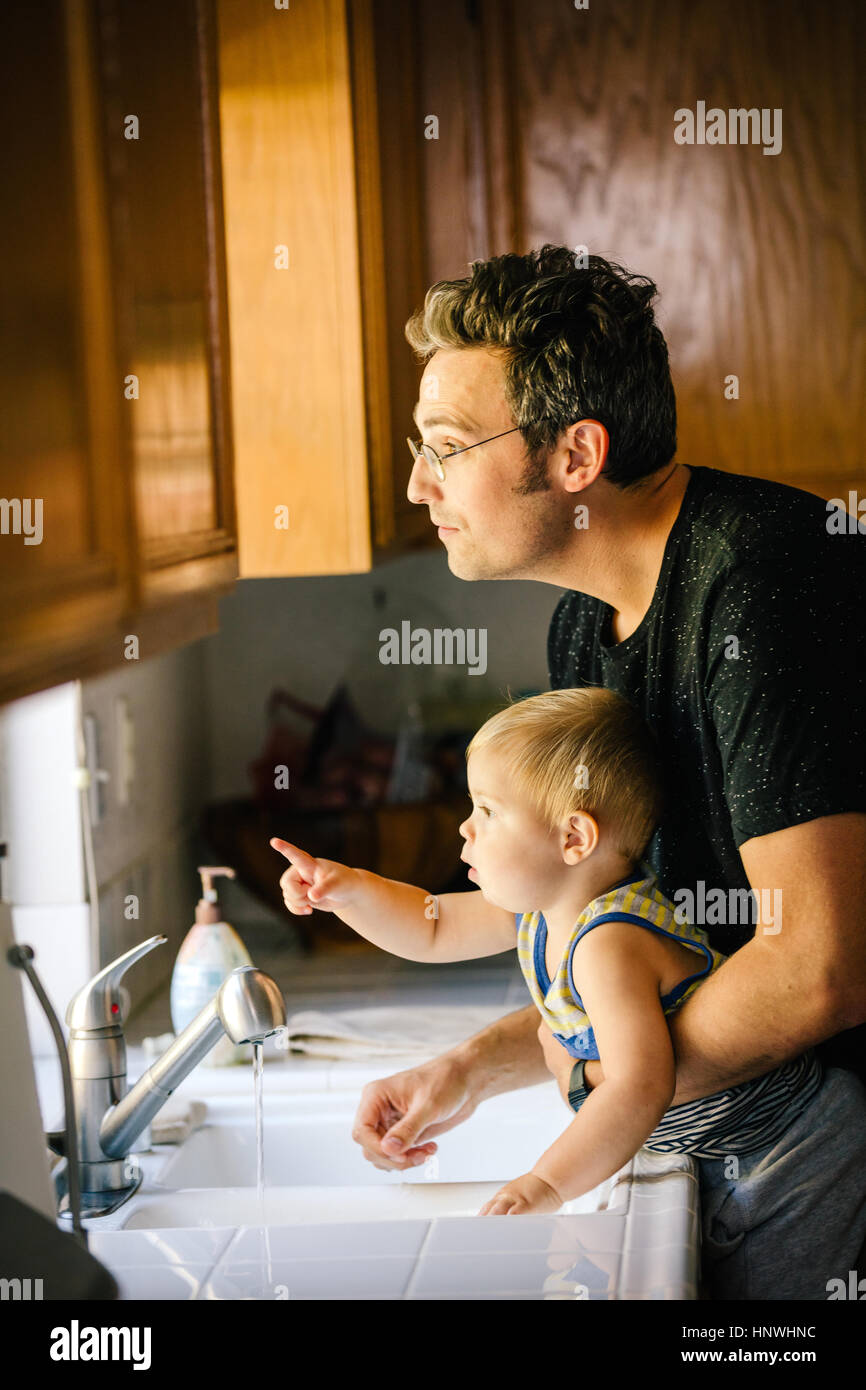 Father and young son washing hands at sink, looking out of window Stock Photo