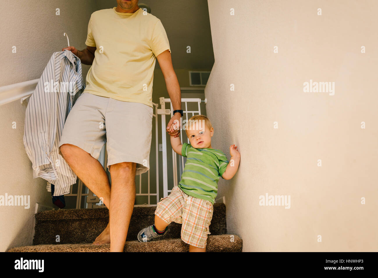 Father and young son walking downstairs, holding hands, father holding shirt on hanger Stock Photo